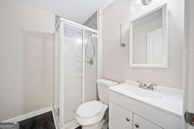 bathroom featuring wood finished floors, toilet, a stall shower, and vanity