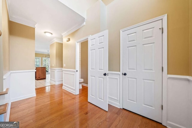 hall featuring a decorative wall, a wainscoted wall, light wood finished floors, and ornamental molding