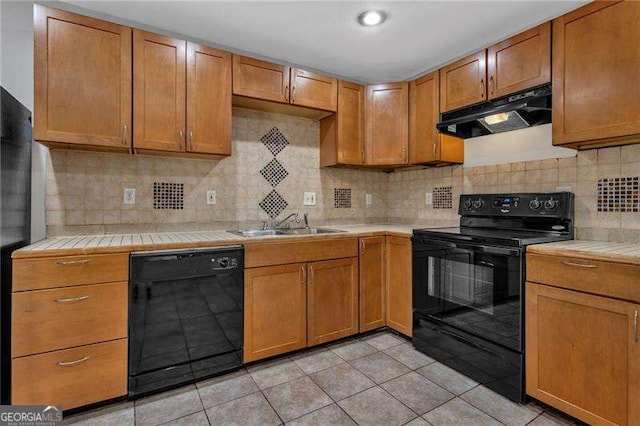 kitchen with a sink, decorative backsplash, black appliances, tile counters, and under cabinet range hood
