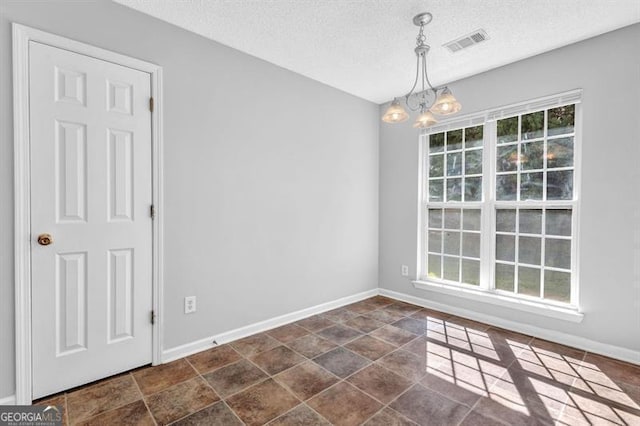 empty room with baseboards, a textured ceiling, visible vents, a notable chandelier, and stone finish flooring
