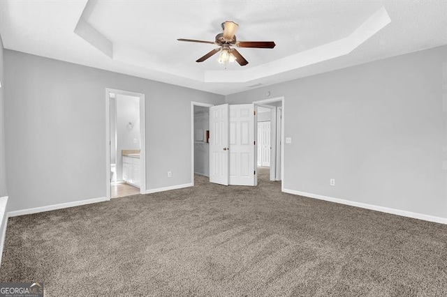 unfurnished bedroom with baseboards, carpet floors, a tray ceiling, and a walk in closet