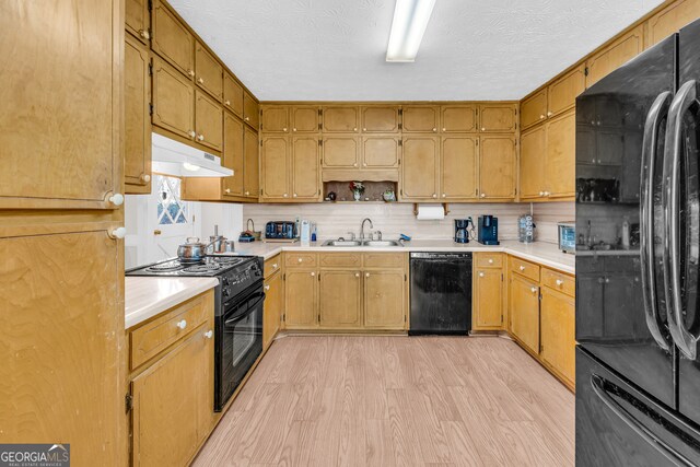 kitchen with light countertops, a sink, light wood-type flooring, under cabinet range hood, and black appliances