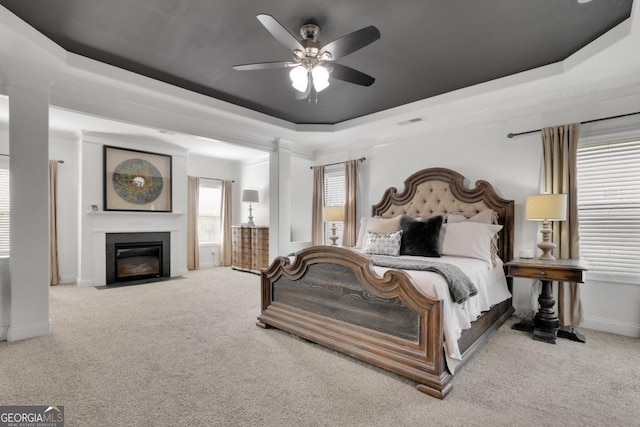 bedroom featuring carpet flooring, a fireplace with flush hearth, a tray ceiling, and visible vents