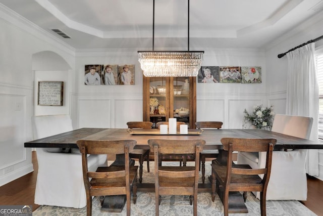 dining area featuring dark wood-style flooring, a decorative wall, and a raised ceiling