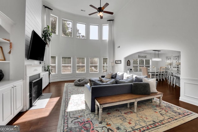 living room featuring dark wood-type flooring, a fireplace with flush hearth, arched walkways, ceiling fan, and a decorative wall
