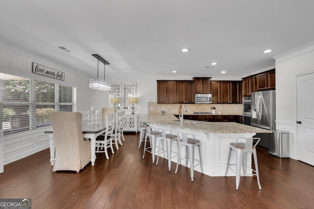kitchen featuring decorative backsplash, a decorative wall, light stone countertops, stainless steel appliances, and dark wood-style floors