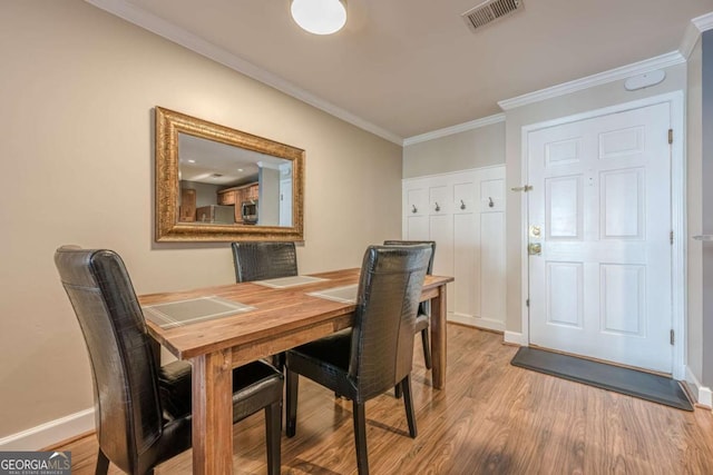 dining area with baseboards, visible vents, ornamental molding, and light wood-style flooring