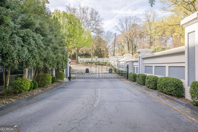 view of street with a gated entry, a gate, and curbs