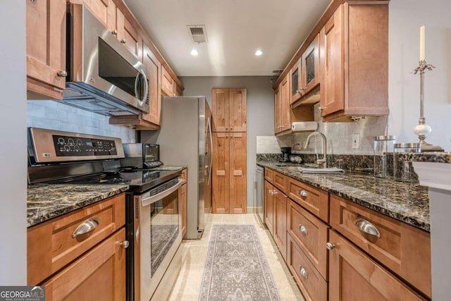 kitchen featuring brown cabinetry, backsplash, visible vents, a sink, and stainless steel appliances