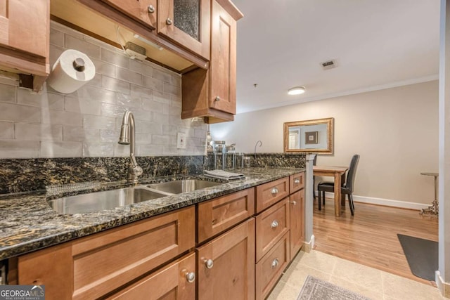 kitchen with crown molding, appliances with stainless steel finishes, a sink, brown cabinetry, and decorative backsplash