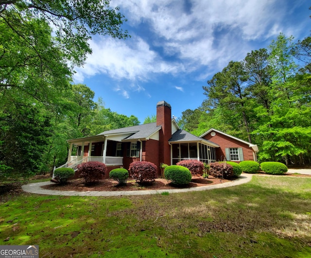 view of home's exterior featuring a chimney, a porch, a yard, roof with shingles, and a sunroom