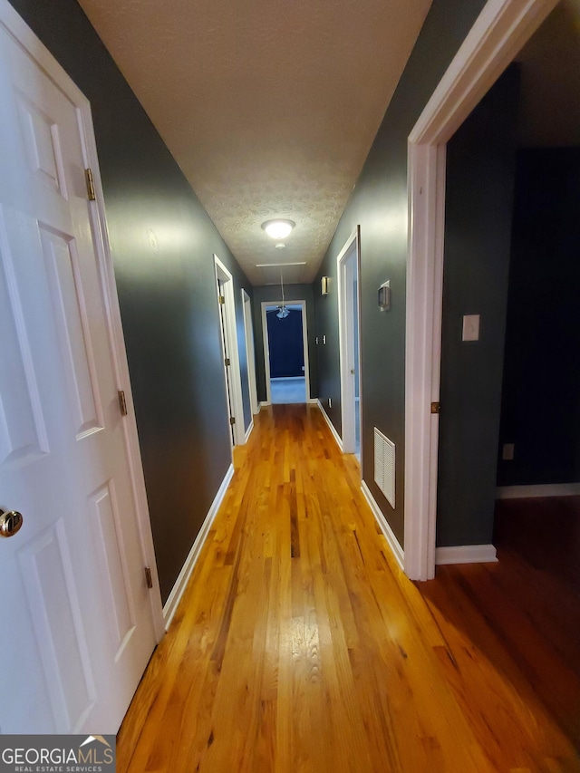 hallway featuring attic access, light wood-type flooring, visible vents, and baseboards