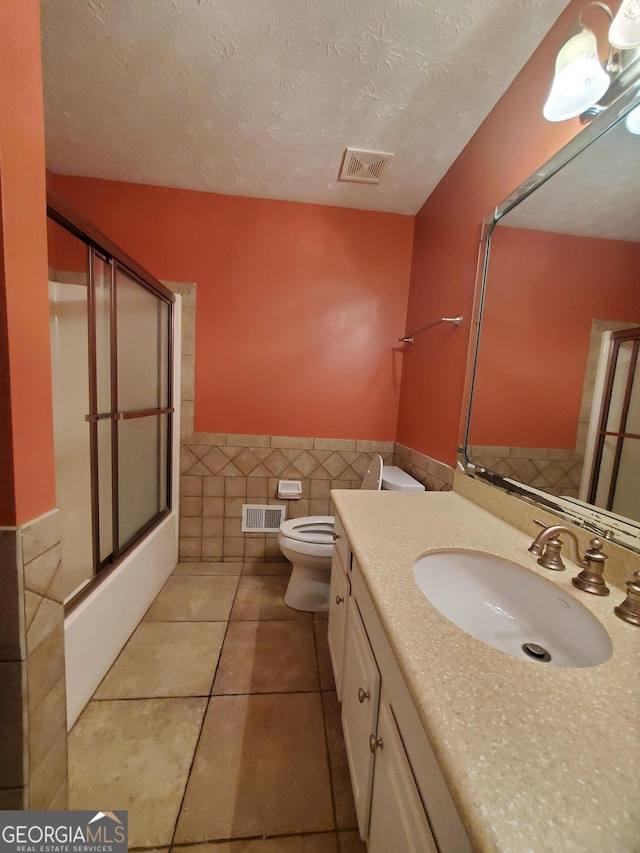 bathroom featuring tile walls, visible vents, toilet, and wainscoting