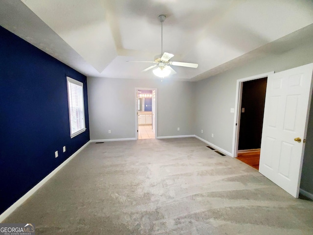 carpeted empty room with a tray ceiling, visible vents, a ceiling fan, and baseboards