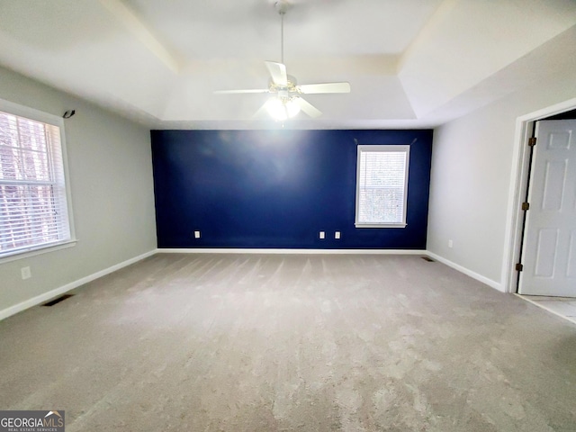 empty room featuring a ceiling fan, visible vents, carpet floors, and a raised ceiling
