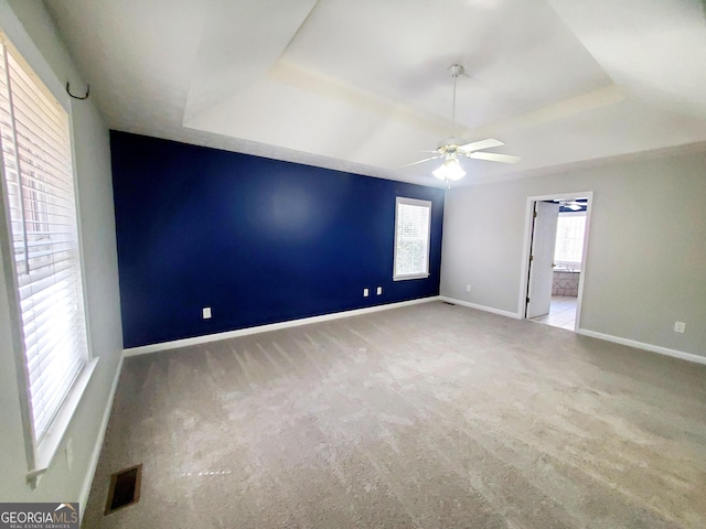 carpeted spare room featuring baseboards, visible vents, a raised ceiling, and plenty of natural light