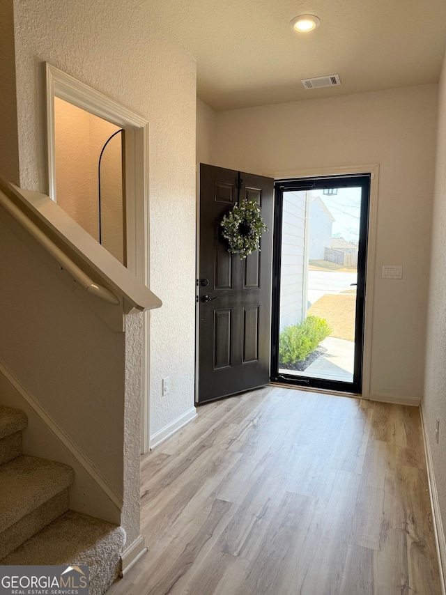 foyer featuring wood finished floors, stairs, baseboards, a textured wall, and recessed lighting