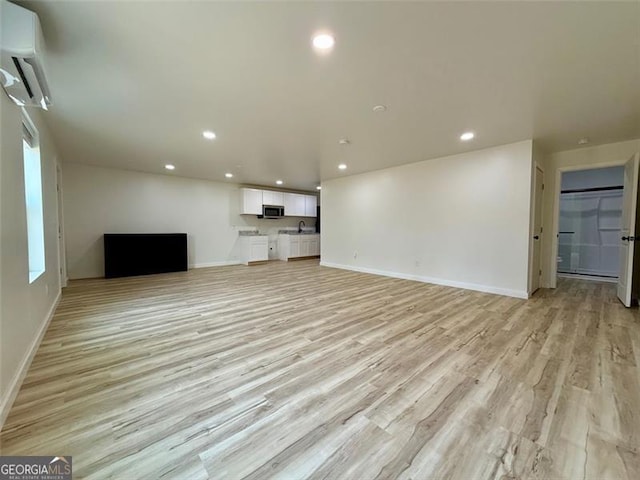unfurnished living room featuring light wood finished floors, a wall unit AC, baseboards, and recessed lighting