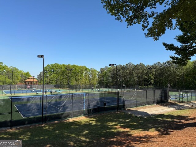 view of tennis court featuring fence and view of wooded area