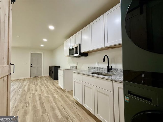 kitchen featuring a sink, stacked washer / drying machine, light stone countertops, light wood finished floors, and white cabinetry