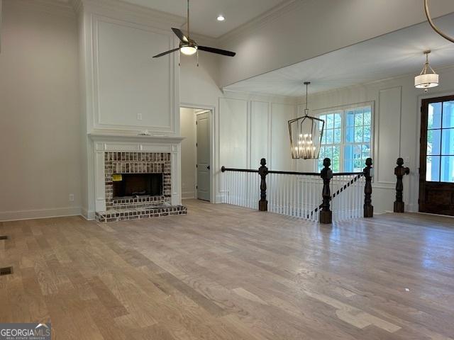 7 Fontaine Dr, Newnan, GA 30263 - unfurnished living room featuring wood finished floors, crown molding, a ceiling fan, a fireplace, and a chandelier