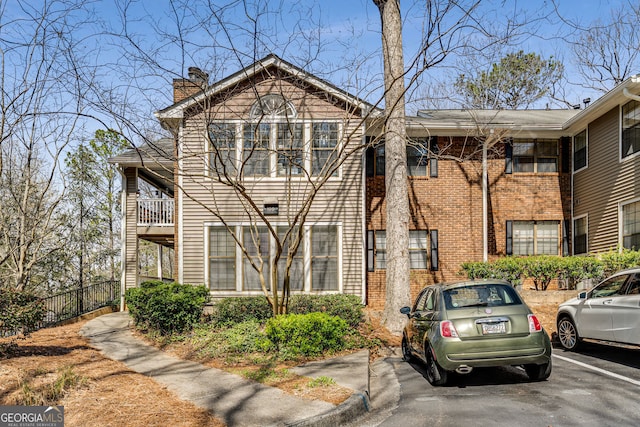 view of front of house featuring brick siding, uncovered parking, a chimney, and fence