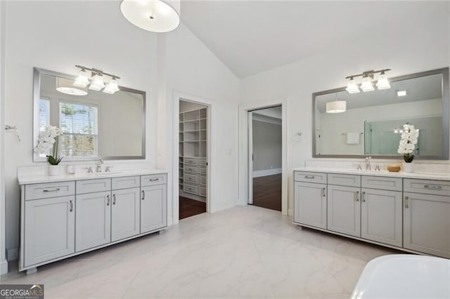 bathroom featuring lofted ceiling, two vanities, and a soaking tub