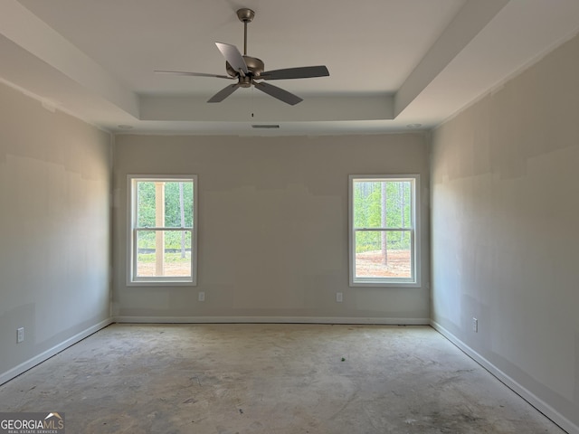 spare room featuring a raised ceiling, baseboards, concrete floors, and a wealth of natural light