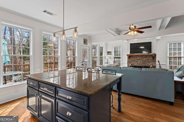 kitchen with ceiling fan, beamed ceiling, a kitchen bar, a fireplace, and wood finished floors