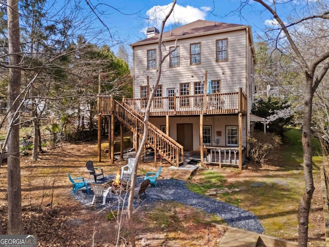 rear view of house with stairs, a wooden deck, a chimney, and an outdoor fire pit