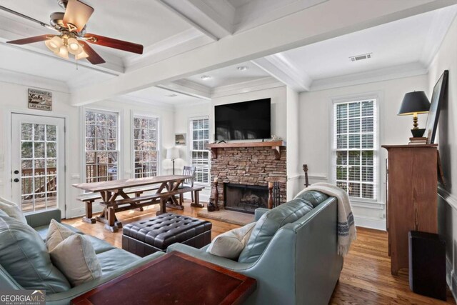 living area featuring a stone fireplace, beam ceiling, crown molding, and wood finished floors