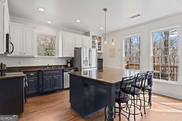 kitchen with a sink, appliances with stainless steel finishes, crown molding, a kitchen breakfast bar, and light wood-type flooring
