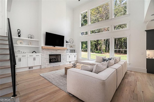 396 Academy St, Alpharetta, GA 30009 - living room featuring a high ceiling, a stone fireplace, stairs, light wood finished floors, and built in shelves