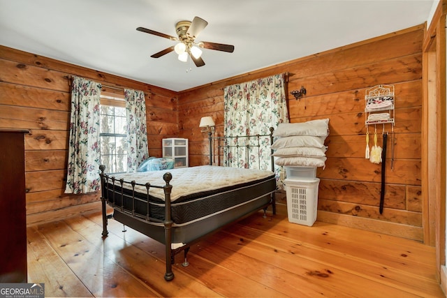 bedroom featuring wood-type flooring, wooden walls, and ceiling fan