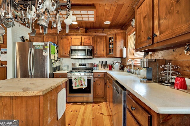 kitchen with butcher block countertops, a sink, appliances with stainless steel finishes, wooden ceiling, and brown cabinetry