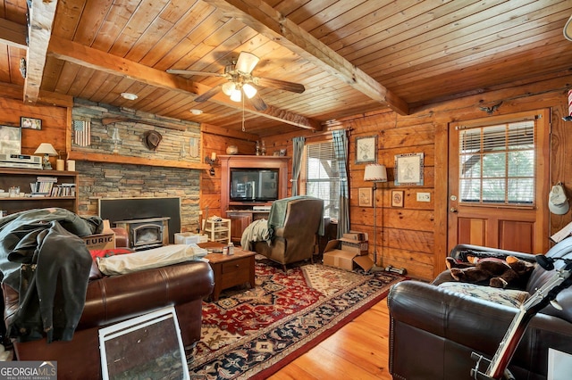 living room featuring beam ceiling, wooden walls, plenty of natural light, and a ceiling fan