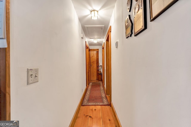 hall with attic access, hardwood / wood-style flooring, and baseboards