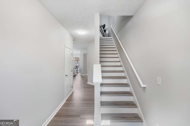 staircase featuring a textured ceiling, baseboards, and wood finished floors