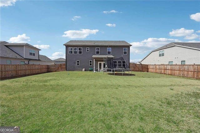 back of property with a fenced backyard, a lawn, and a trampoline