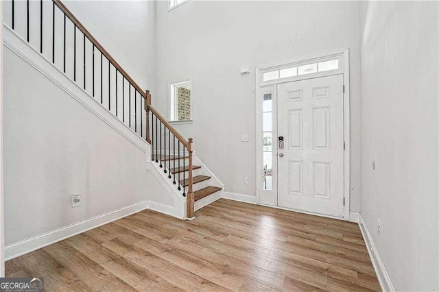entryway featuring light wood-type flooring, baseboards, a high ceiling, and stairs