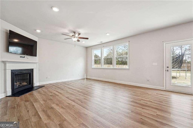 unfurnished living room featuring a glass covered fireplace, baseboards, light wood-style floors, and a ceiling fan