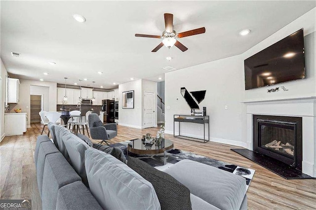 living room with a ceiling fan, baseboards, and light wood finished floors