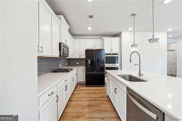kitchen featuring a sink, white cabinets, appliances with stainless steel finishes, light wood-type flooring, and backsplash