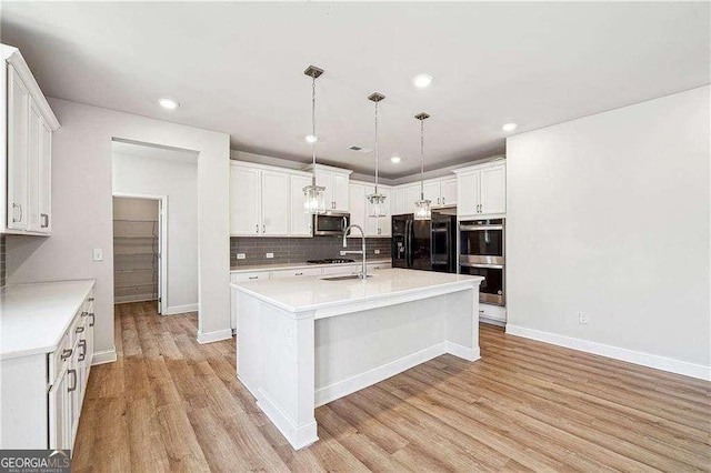 kitchen with black appliances, light wood-style floors, white cabinets, light countertops, and decorative backsplash