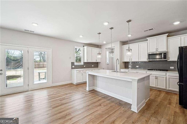 kitchen featuring light wood-style flooring, freestanding refrigerator, a sink, light countertops, and stainless steel microwave