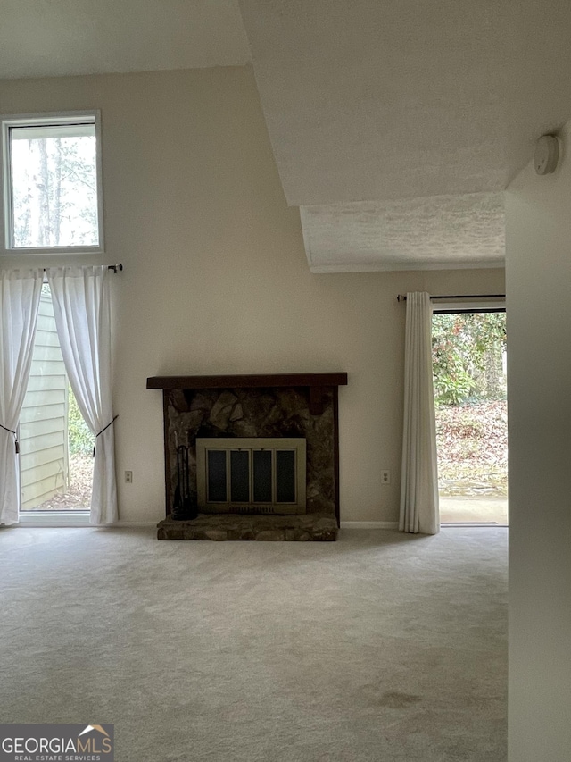 unfurnished living room featuring carpet floors, a stone fireplace, and healthy amount of natural light