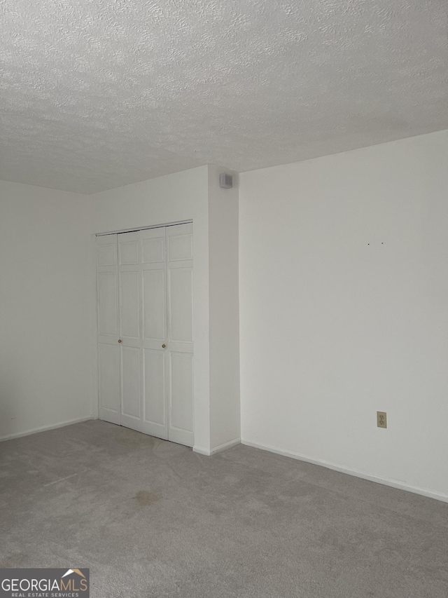 unfurnished bedroom with a textured ceiling, a closet, carpet flooring, and baseboards
