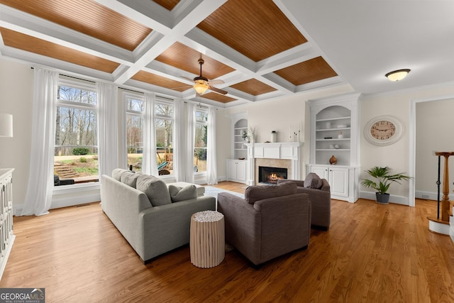 living area with a ceiling fan, baseboards, a warm lit fireplace, ornamental molding, and light wood-type flooring