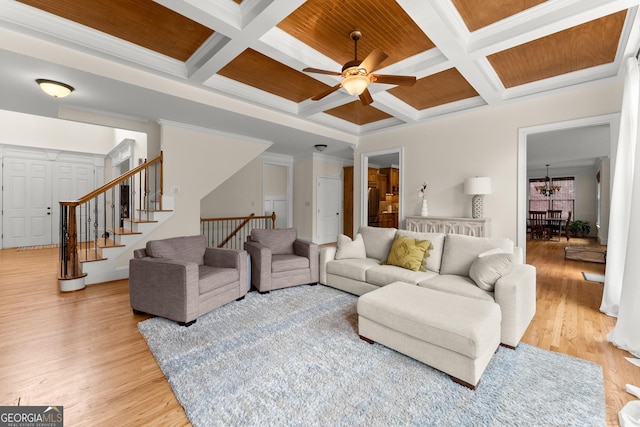 living area with ornamental molding, beam ceiling, ceiling fan with notable chandelier, light wood-style floors, and coffered ceiling