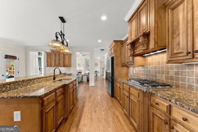 kitchen featuring brown cabinets, a sink, dark stone countertops, appliances with stainless steel finishes, and crown molding